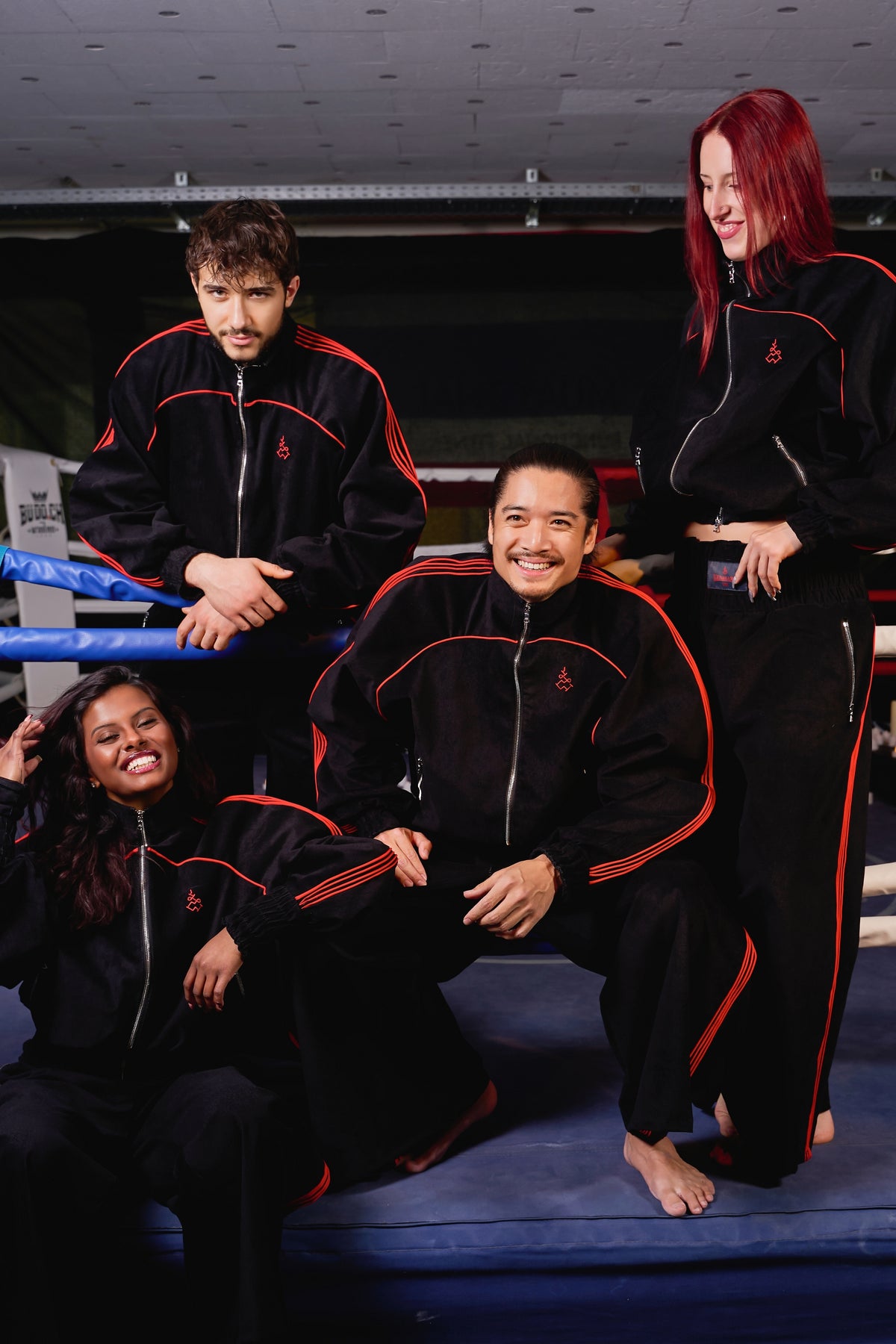 Four people in matching black and red tracksuits posing together in a gym. Muay Thai Streetwear Sak Yant Tattoo Thai Boxing Tracksuit Muay Thai Lienhard VIII