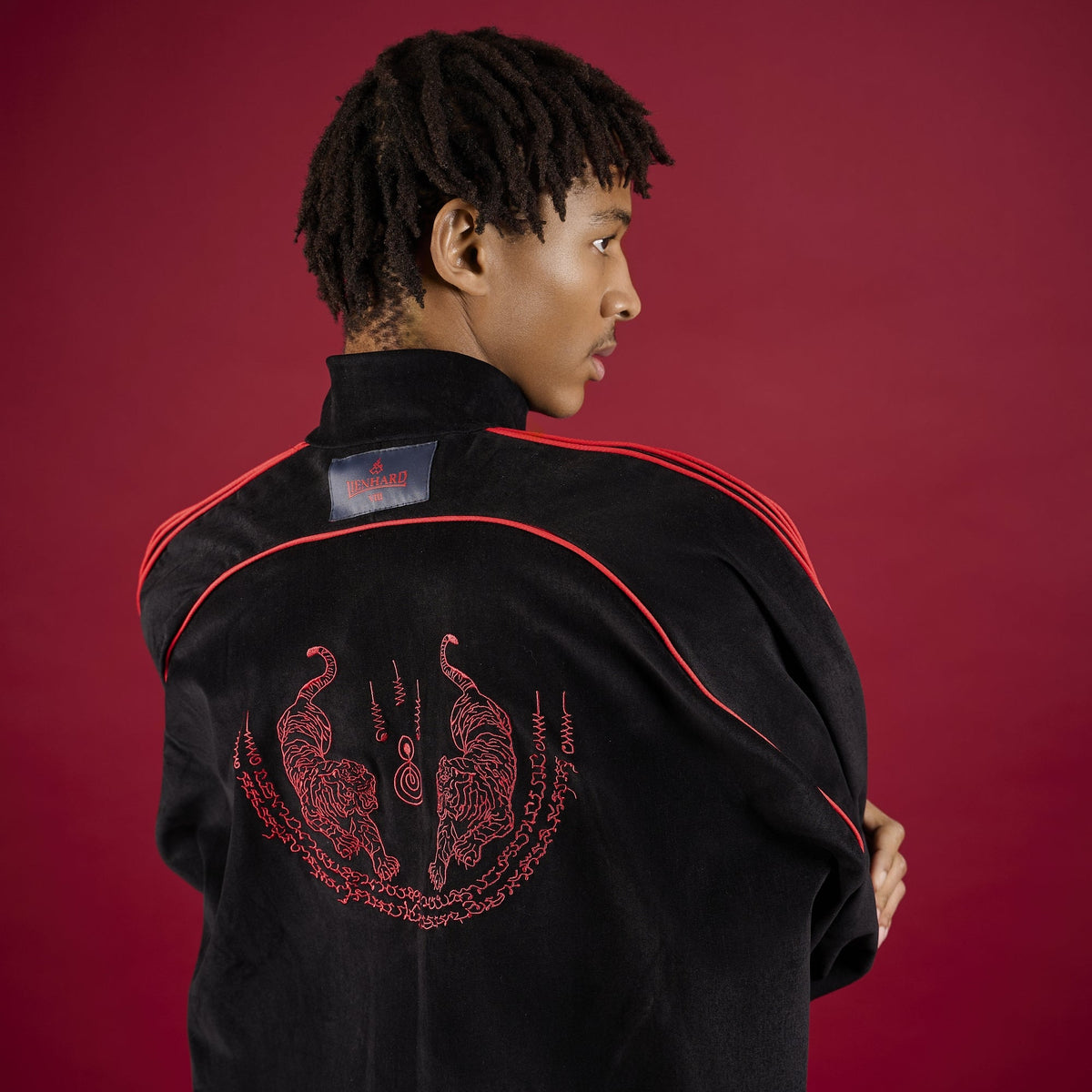 Person wearing a black tracksuit with red accents on a red background Lienhard VIII Muay Thai Streetwear Jacket Tracksuit Sak Yant Jacket
