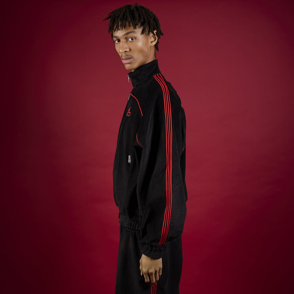 Person wearing a black tracksuit with red accents on a red background Lienhard VIII Muay Thai Streetwear Jacket Tracksuit Sak Yant Jacket