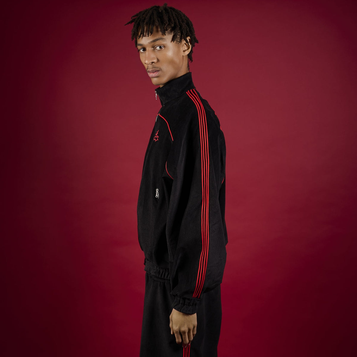 Person wearing a black tracksuit with red accents on a red background Lienhard VIII Muay Thai Streetwear Jacket Tracksuit Sak Yant Jacket