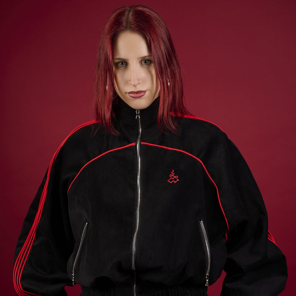 Person wearing a black tracksuit with red accents on a red background