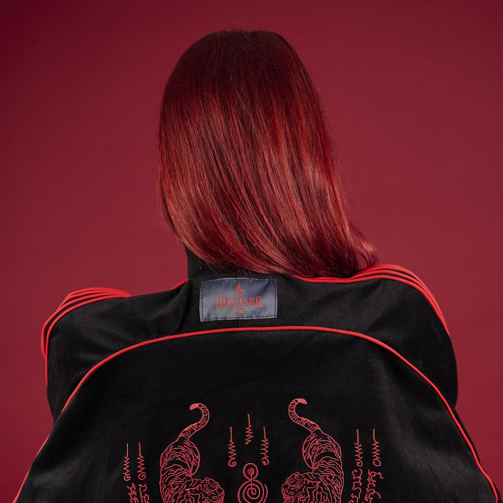 Person wearing a black jacket with red embroidery on a red background