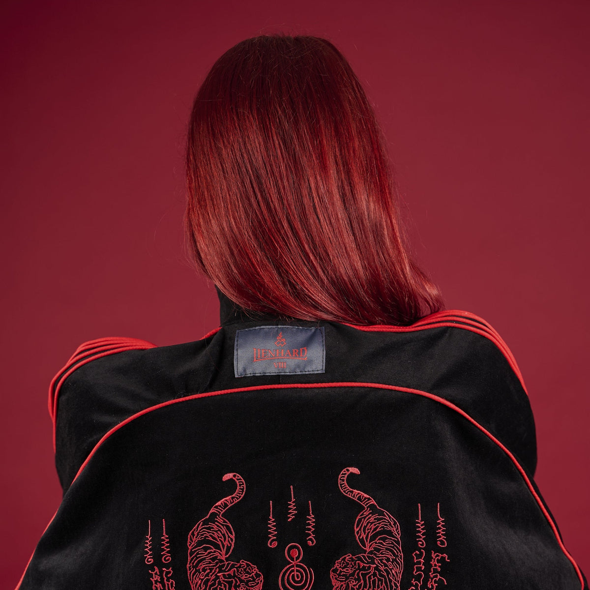 Person wearing a black jacket with red embroidery on a red background