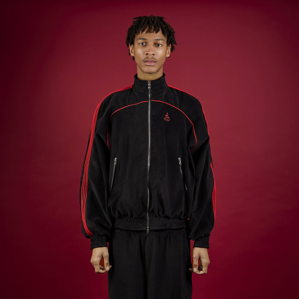 Person wearing a black tracksuit with red accents on a red background Lienhard VIII Muay Thai Streetwear Jacket Tracksuit Sak Yant Jacket